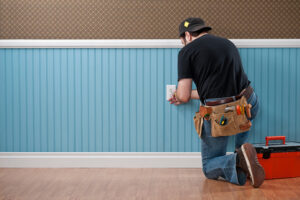 Man with a tool belt crouching down to install a wall outlet.